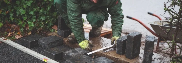Person verlegt Pflastersteine mit Richtscheit.
